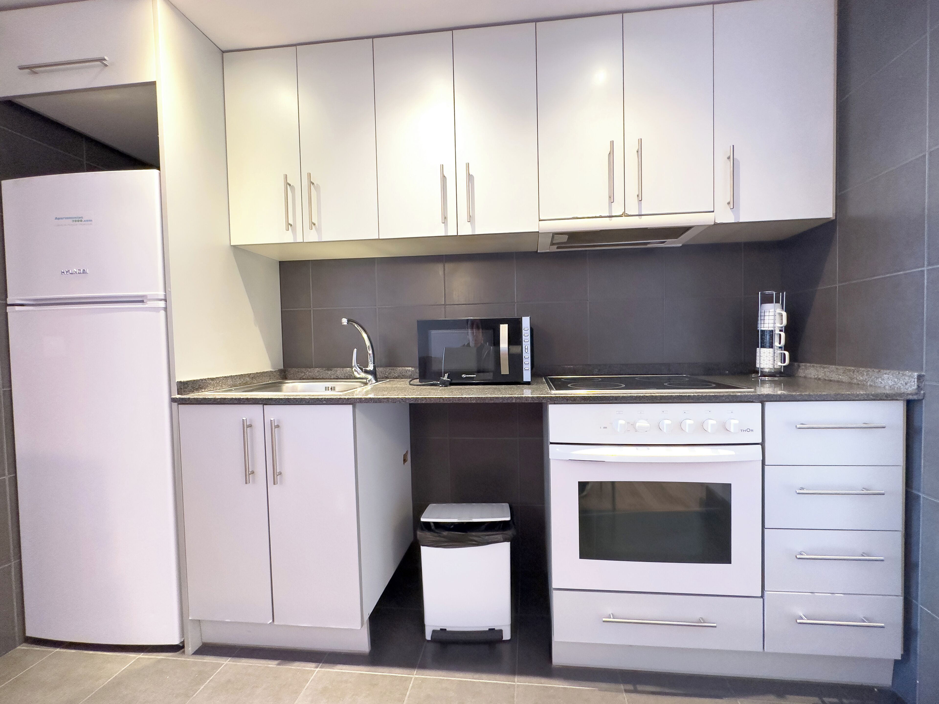 A modern kitchen with white cabinets, a stainless steel sink, a microwave, and a built-in oven.