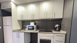 A compact kitchen with white cabinets, a built-in microwave, a coffee maker, and a stove.