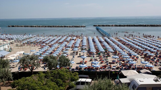 Une plage bordée de rangées de parasols bleus et blancs, une jetée et une digue rocheuse.