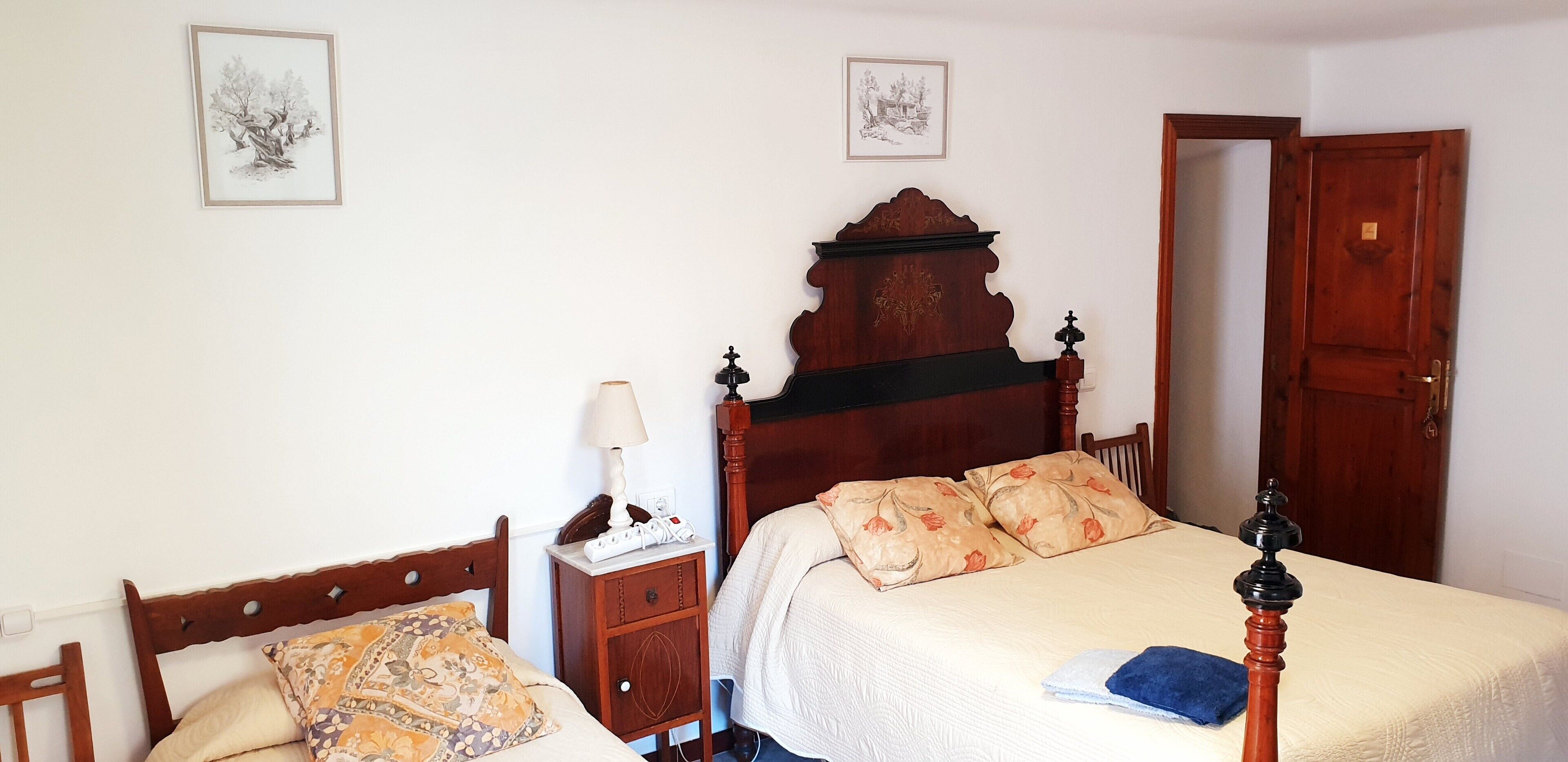 A bedroom with a wooden bed, a bedside table with a lamp, and two framed pictures on the wall.