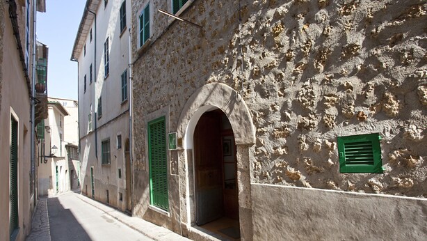 Una calle estrecha con edificios de muros de piedra y contraventanas verdes.
