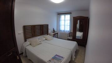 Ein Schlafzimmer mit einem großen Bett, einem Holzkopfende, einem Nachttisch mit Lampe, einem Fenster mit Vorhängen und einem Spiegel.