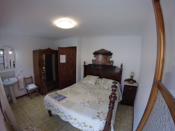 A bedroom with a wooden bed, a nightstand, a mirror, a wooden wardrobe, and a bathroom with a sink and chair.