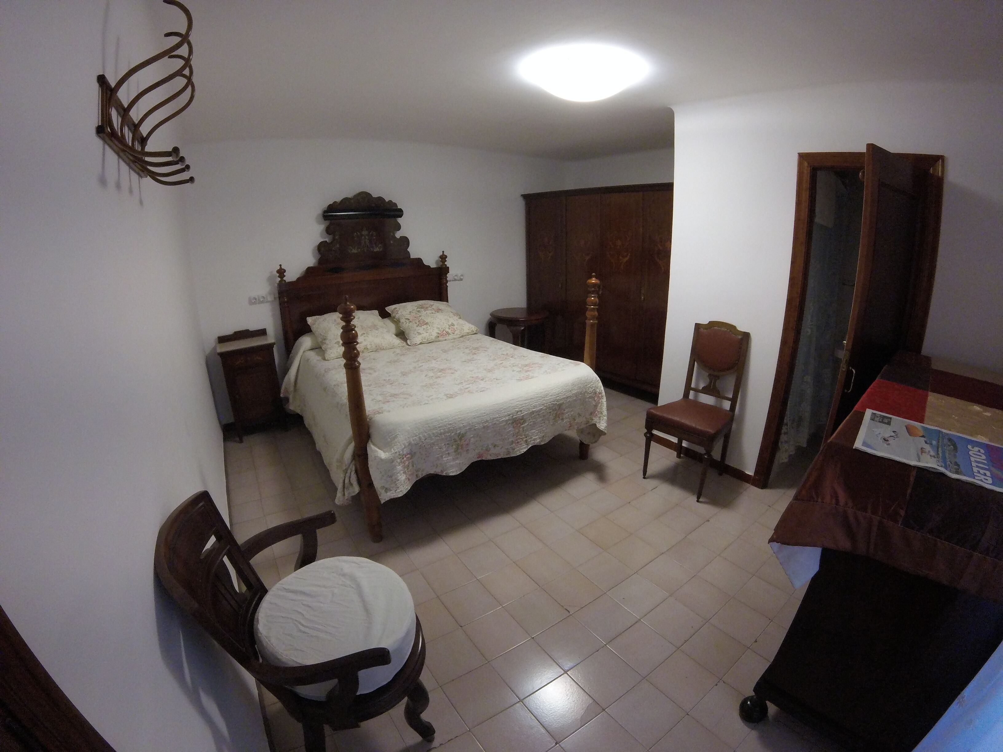 Une chambre à coucher avec un lit en bois, une chaise en bois, une table de chevet, une armoire et une petite table sur laquelle se trouve un magazine.