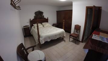 Un dormitorio con una cama y una silla de madera, una mesita de noche, un armario y una pequeña mesa con una revista.
