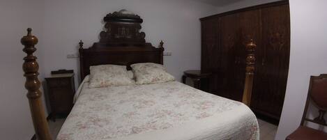 A bedroom with a wooden bed frame, floral bedding, a nightstand, a wardrobe, and a chair.