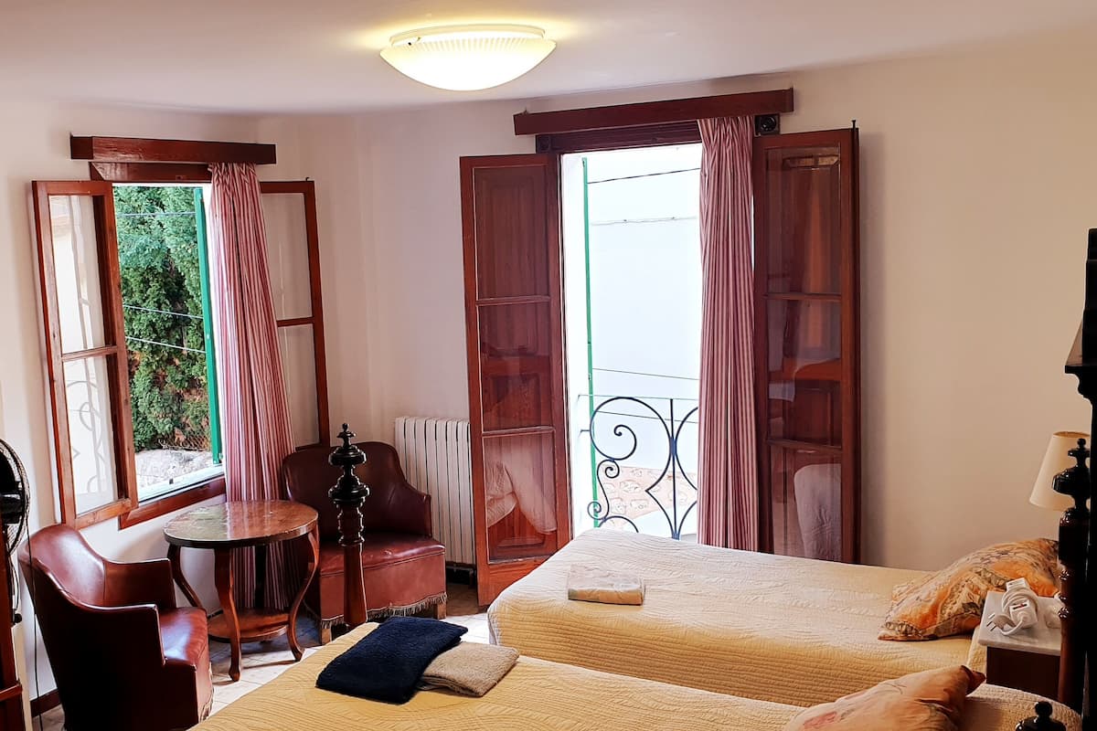 Quarto de hotel com duas camas, um guarda-roupa de madeira, uma mesinha e uma cadeira.