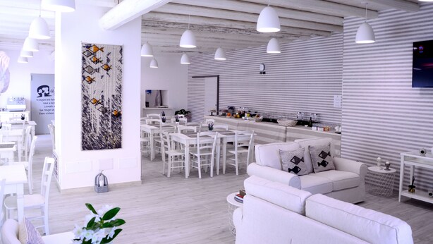 Un intérieur moderne aux tons clairs, avec un espace repas, des canapés blancs et des luminaires suspendus.
