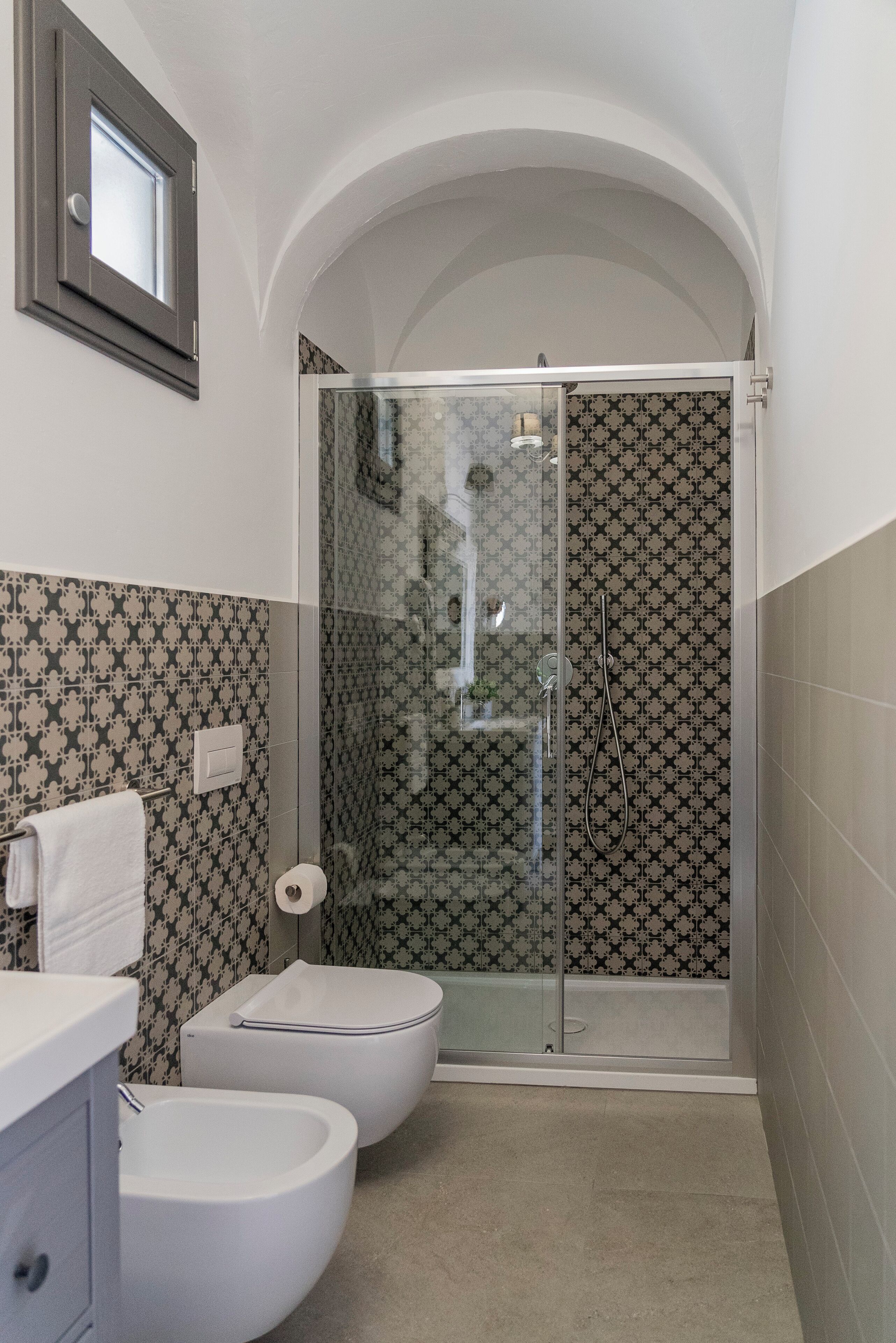 A bathroom with a shower, toilet, bidet, and a small window.
