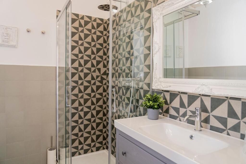A modern bathroom with a geometric patterned shower wall, a white sink with a mirror, and a small potted plant.