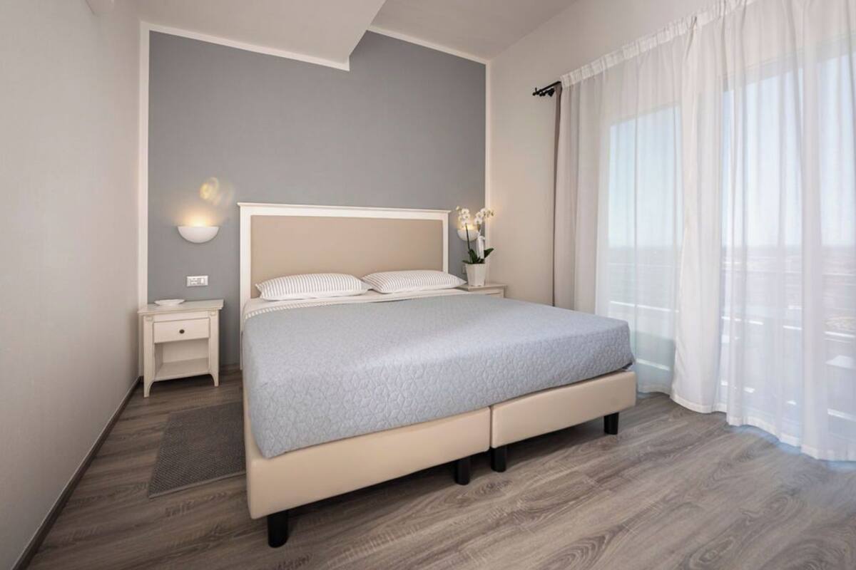 Ein modernes Schlafzimmer mit Bett, Nachttisch, Lampe und Vorhängen.