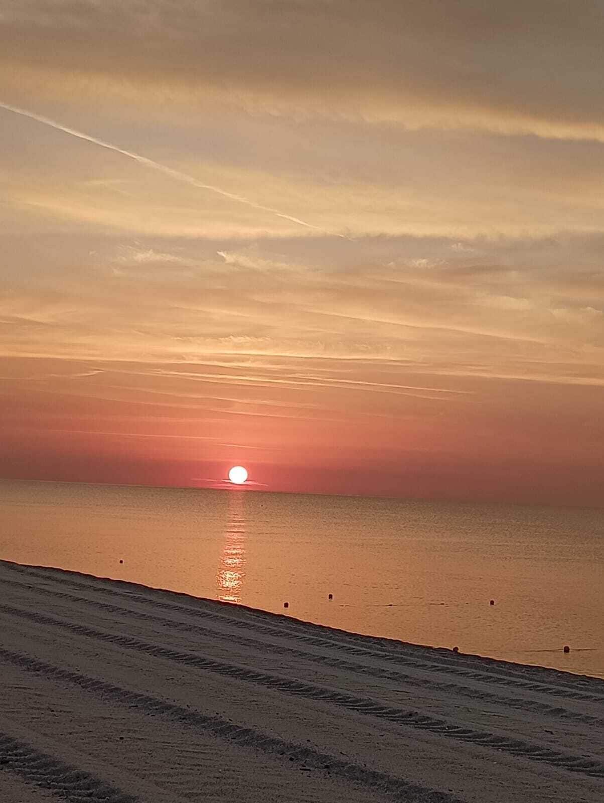 A sunset over a beach with a clear sky and calm sea.