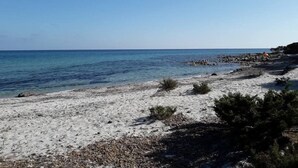 Une plage de sable fin bordée d’une eau d’un bleu limpide et parsemée de rochers.