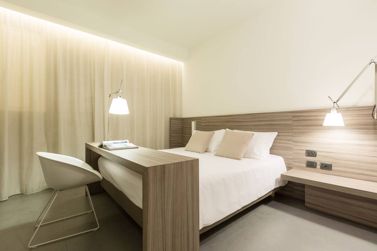 A modern hotel room with a bed, bedside tables, a desk, and a chair.