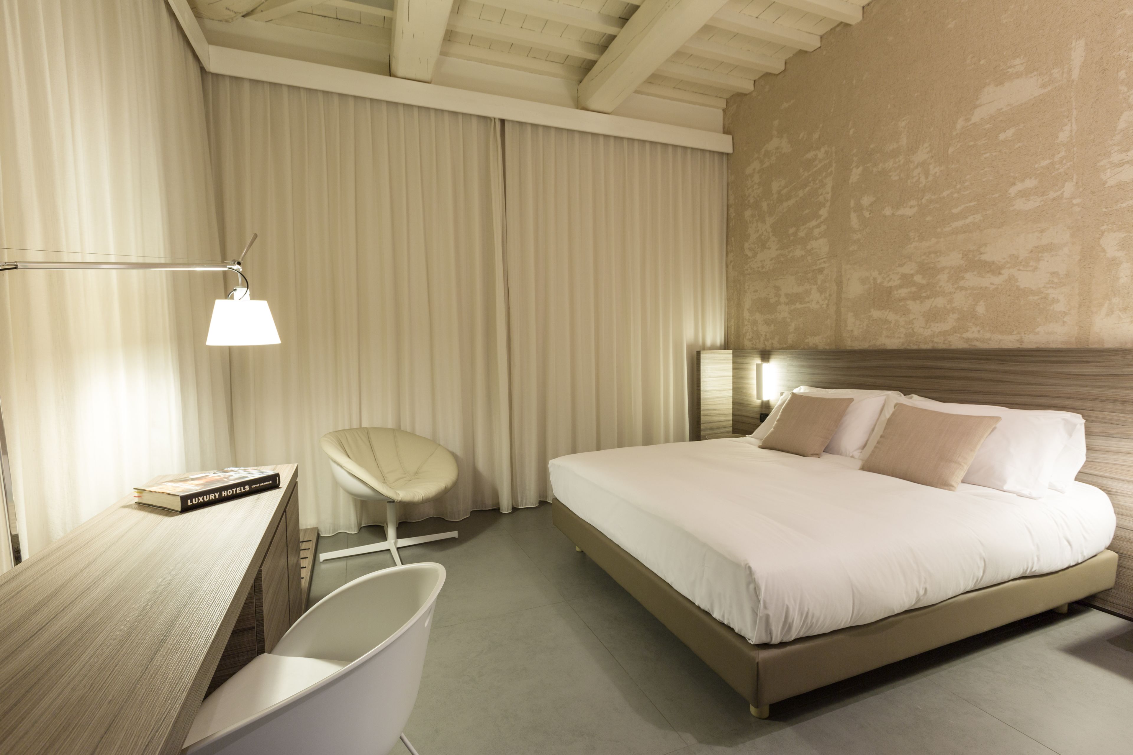 A modern hotel room with a large bed, a desk, a chair, and a lamp.