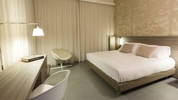 A modern hotel room with a large bed, a desk, a chair, and a lamp.