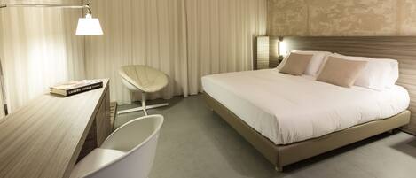 A modern hotel room with a large bed, a desk, a chair, and a lamp.