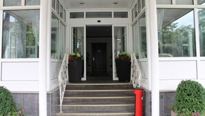A building entrance with a staircase, large windows, and potted plants. - City Hotel Kassel (Kassel)