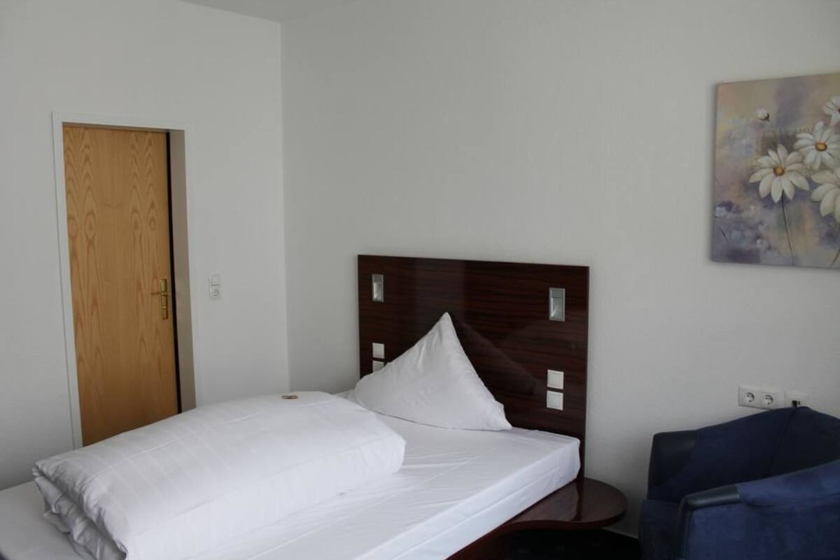 A neatly made bed with white linens in a room with a wooden door and a painting of flowers on the wall.