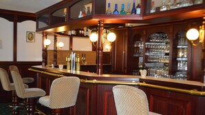 A bar area with wooden bar counter, two bar stools, and shelves with bottles and glasses. - City Hotel Kassel (Kassel)