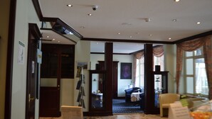 A hotel lobby with a marble floor, a reception desk, a seating area with a sofa and armchairs, and a large mirror. - City Hotel Kassel (Kassel)