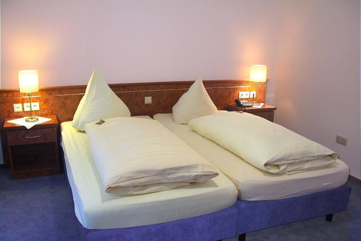 A double bed with two pillows, a wooden headboard, and bedside lamps.