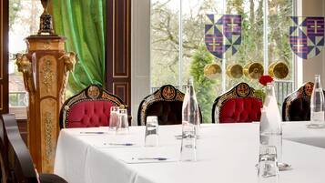 A formal dining room with ornate chairs, a table set for a meal, and a view through large windows.