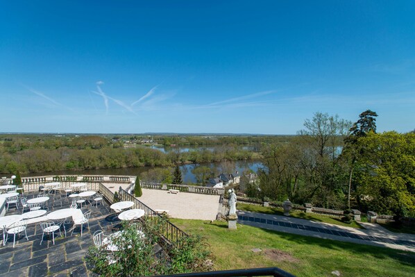 A terrace with outdoor seating overlooking a lake and a statue. - Château Le Prieuré - La Maison Younan (Gennes-Val-de-Loire)