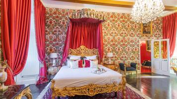 Une chambre à coucher luxueuse, avec un grand lit richement décoré, des rideaux rouges et un papier peint à motifs floraux.