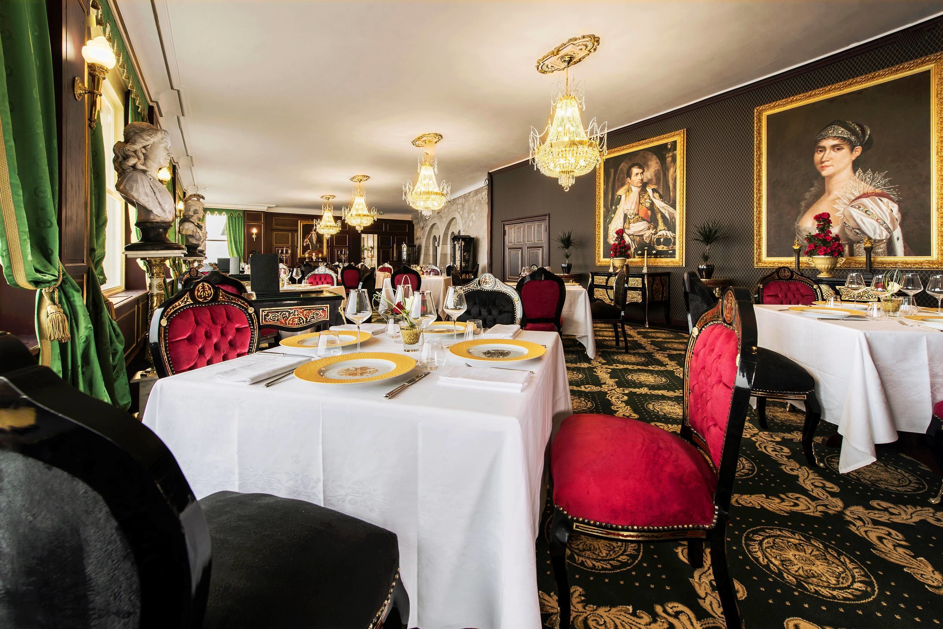 Un comedor elegante con varias mesas, sillas tapizadas en rojo y candelabros.