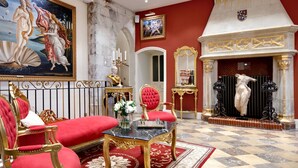 A luxurious room with red upholstered chairs, a marble coffee table, and a fireplace with a statue.