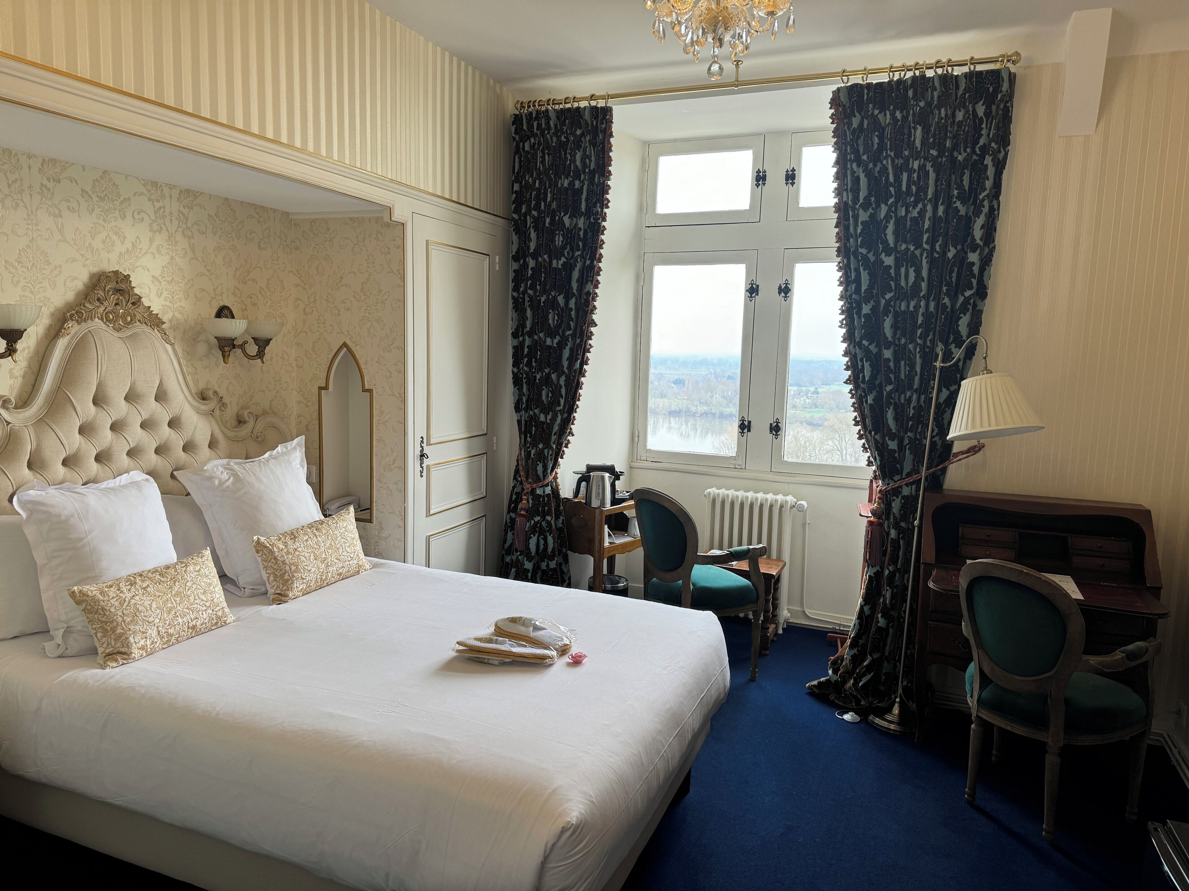 A hotel room with a large bed, a desk, a chair, a radiator, and a view of the outdoors.