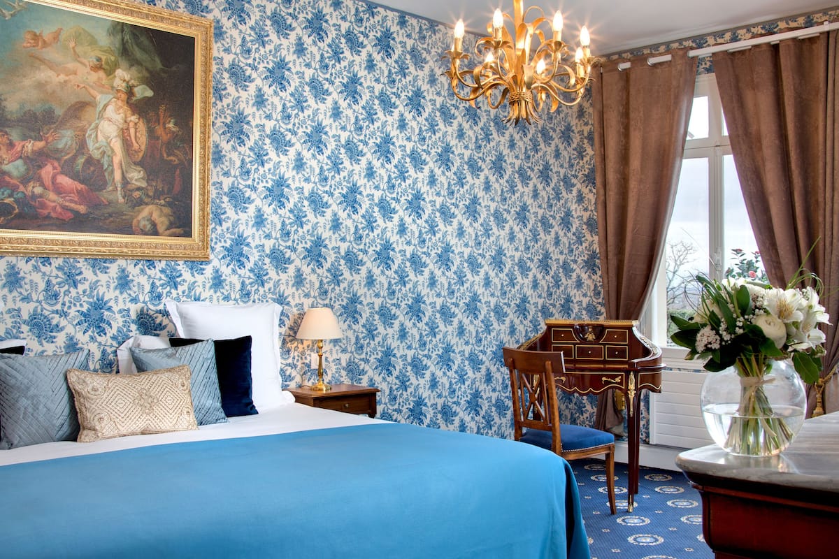Een slaapkamer met een groot bed, nachtkastje, bureau, stoel en een kroonluchter.