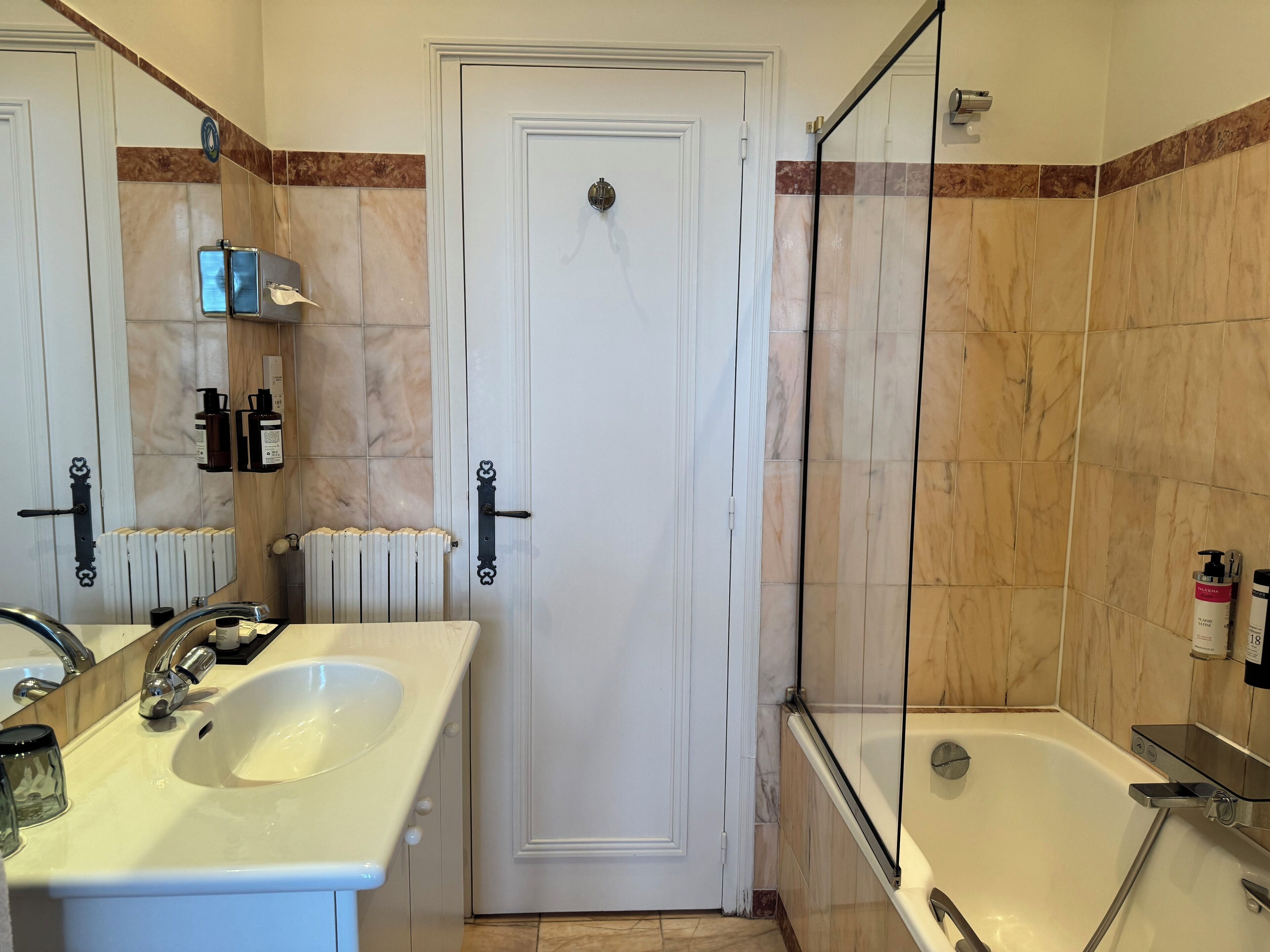 A bathroom with a white sink, a mirror, a door, and a glass-enclosed shower.