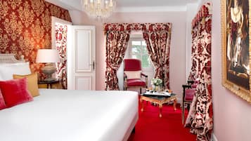 Ein Zimmer mit einem großen Bett, einer Kristallleuchtre, einem roten Sessel und einem Gemälde an der Wand.