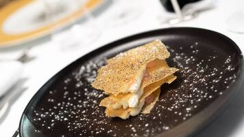 A dessert on a black plate with powdered sugar, accompanied by a fork and a knife on the table.