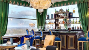 A bar area with a view of the city, bar stools, and a chandelier.