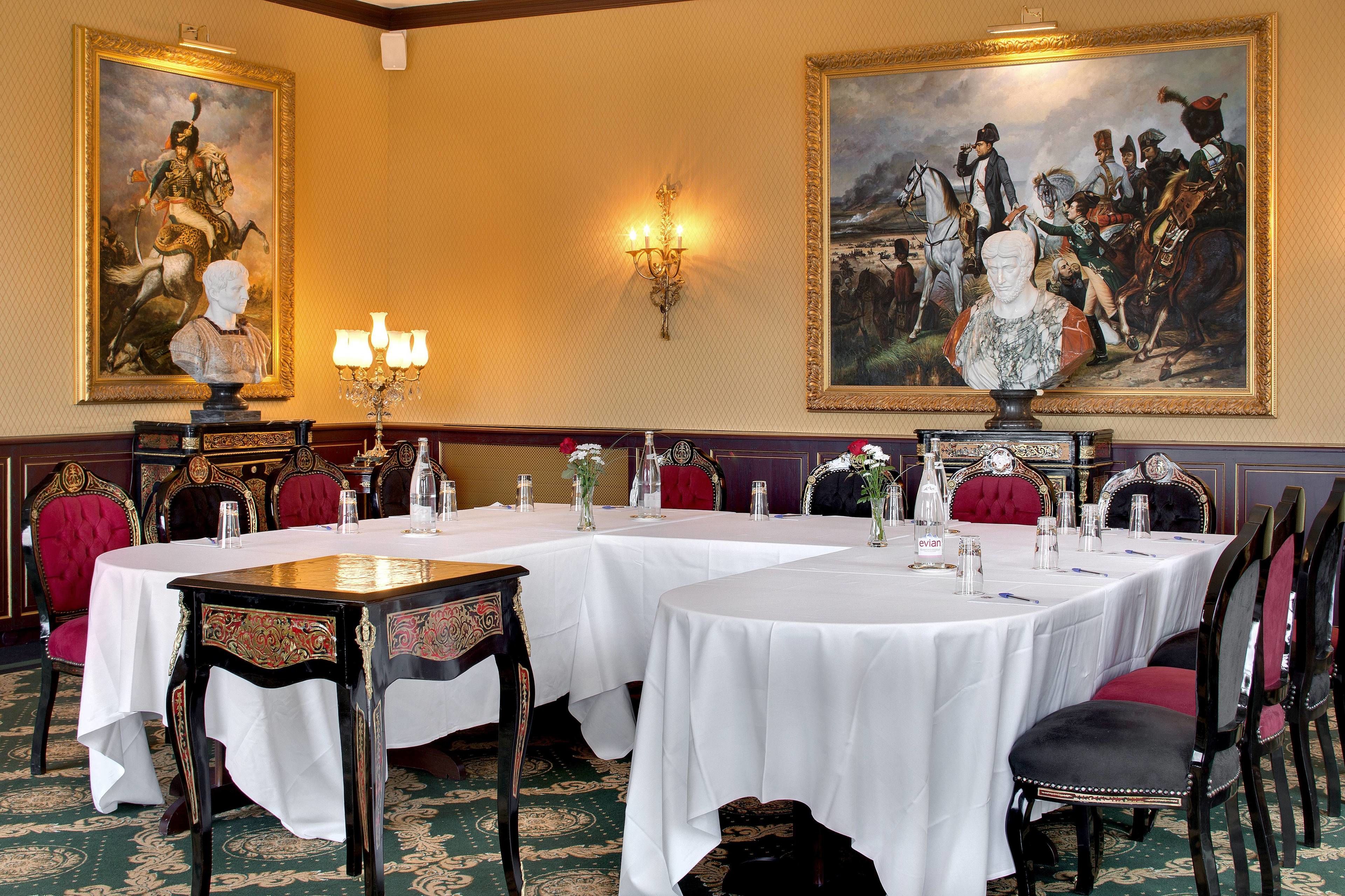 Une salle à manger élégante, avec des tables dressées pour le repas, entourée de fauteuils richement décorés et de tableaux accrochés aux murs.