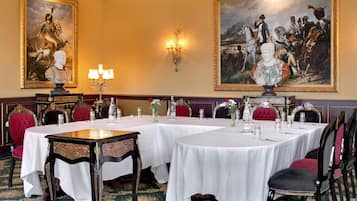 Un comedor formal con mesas dispuestas para una comida, rodeado de sillas ornamentadas y cuadros en las paredes.