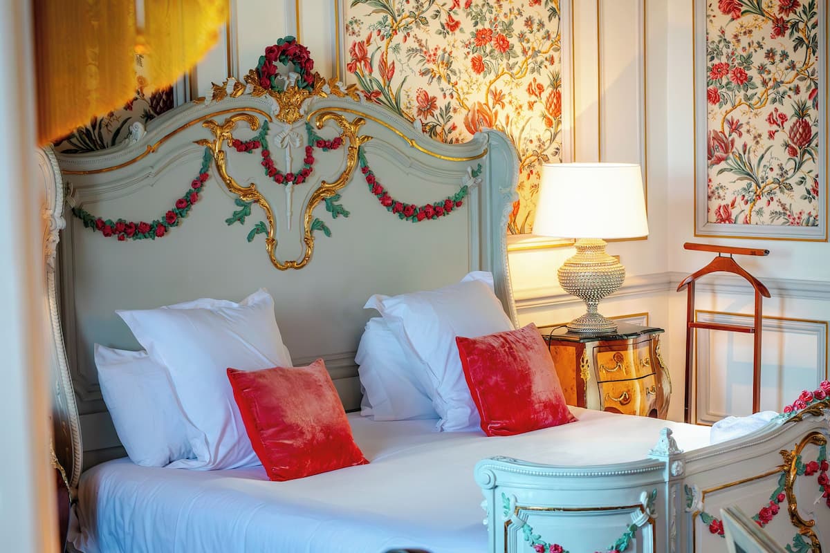 Een slaapkamer met een bed, nachtkastje, lamp en bloemenbehang.