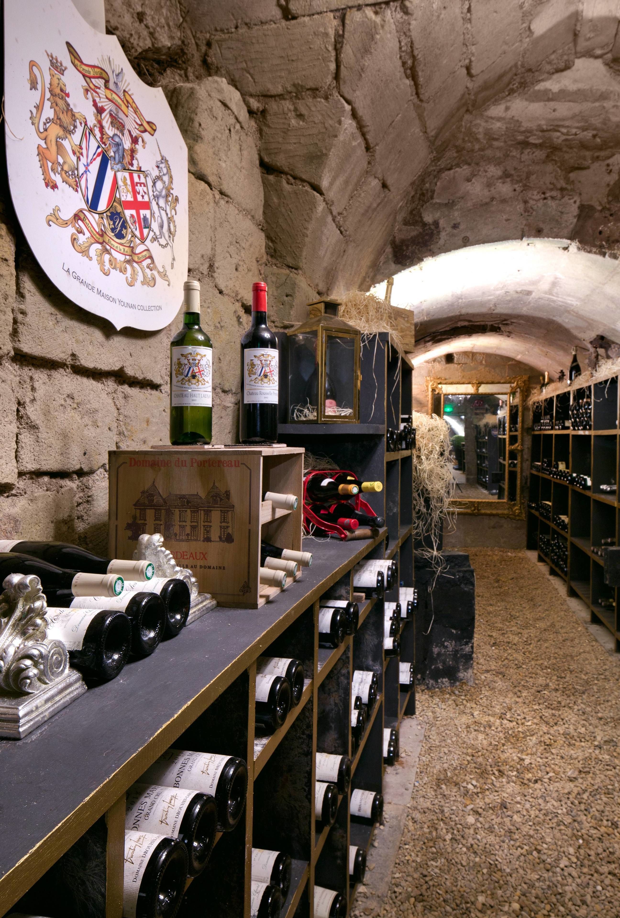 A wine cellar with wooden shelves and bottles, a coat of arms on the wall, and a gravel floor.