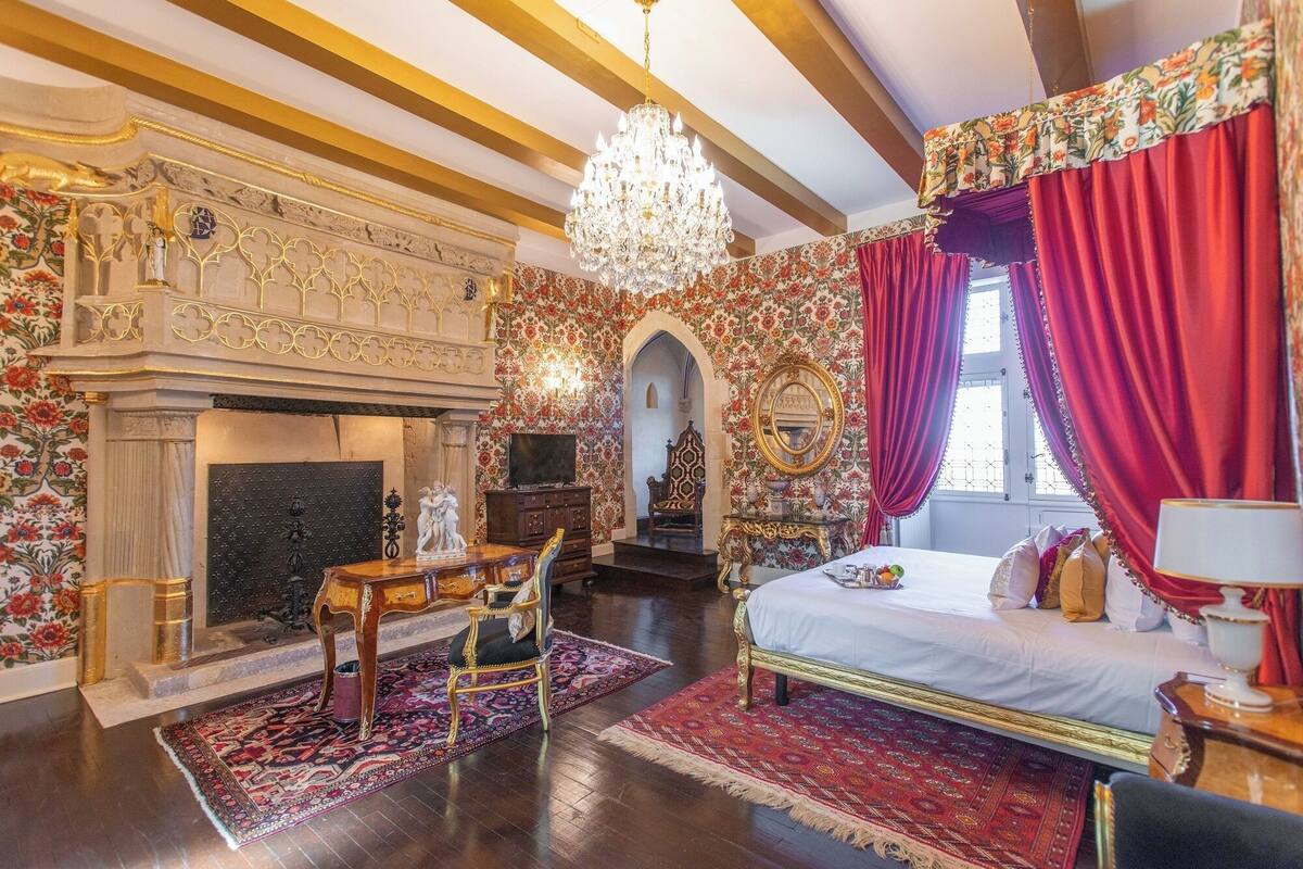 Een luxueuze slaapkamer met een groot bed, een decoratieve open haard en bloemenbehang.