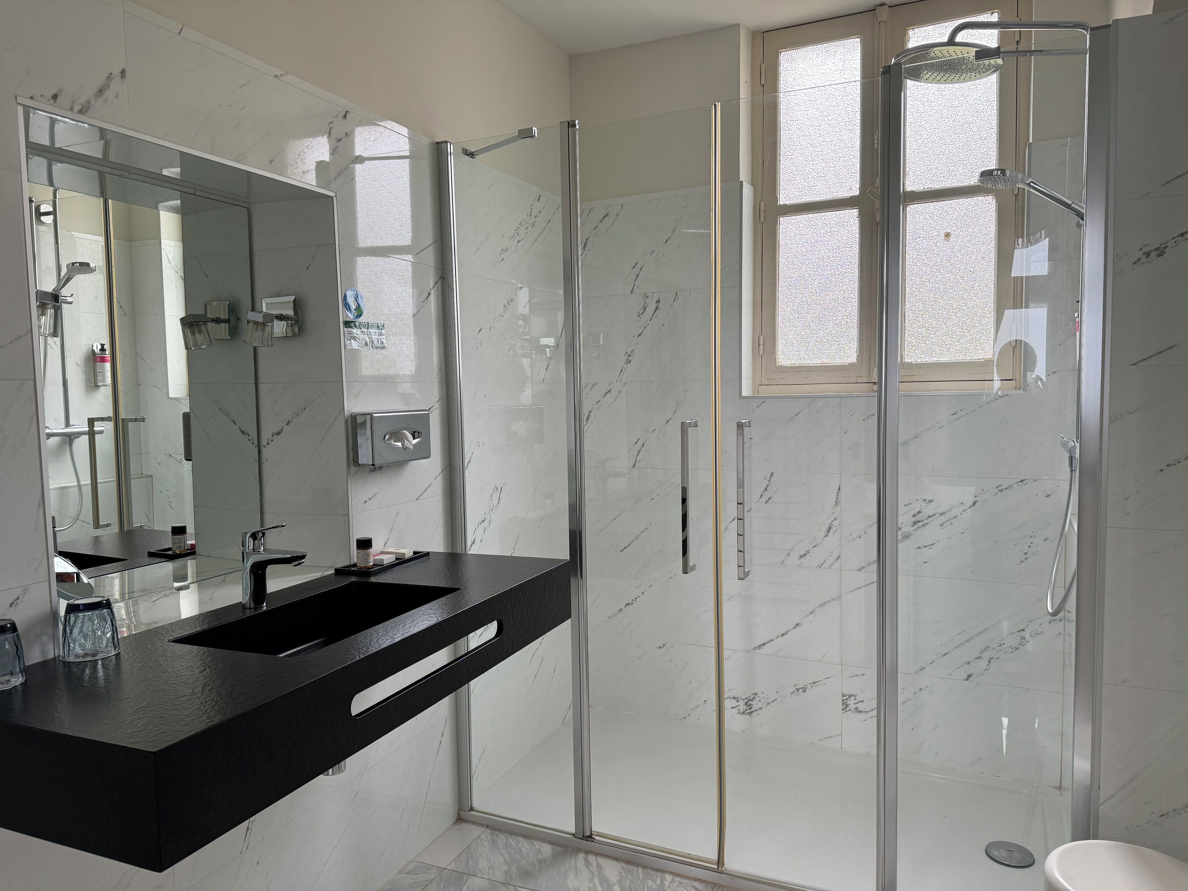 A modern bathroom with a glass-enclosed shower, a large mirror, and a black countertop.
