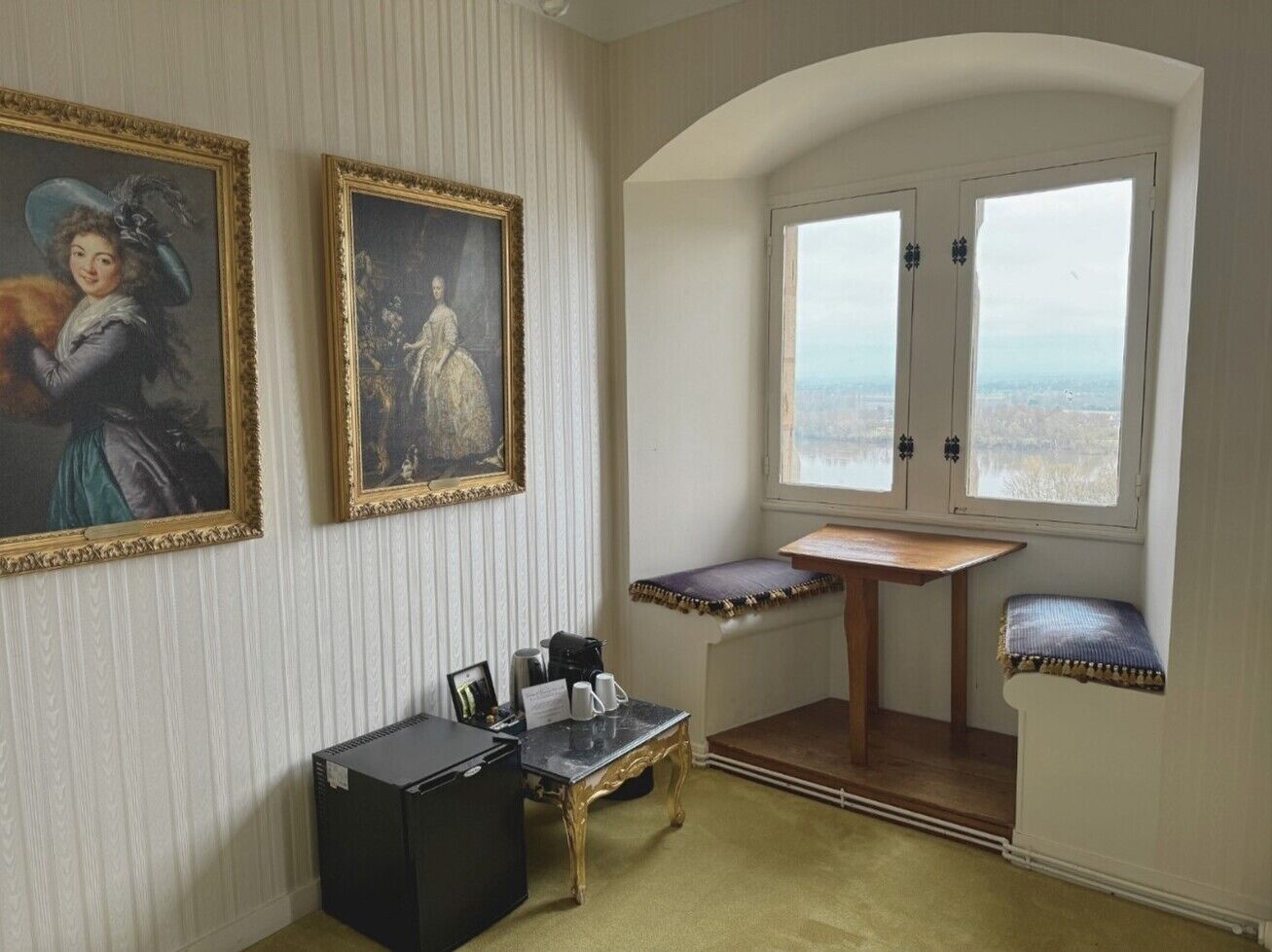 A room with two framed paintings, a small table with a bench, and a view through a door.