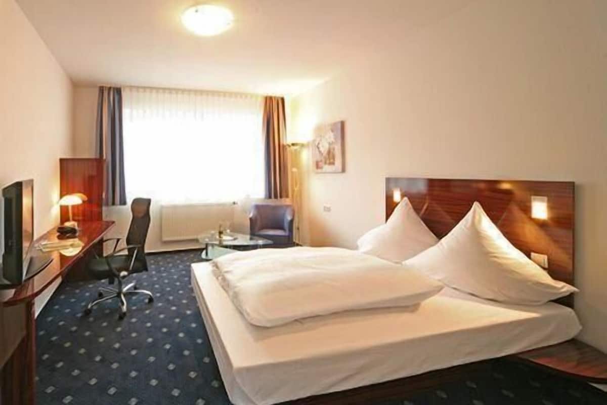 A hotel room with a large bed, a desk with a computer, a chair, and a television.