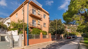 Un edificio de varios pisos con balcones, una entrada con reja y vista a la calle con automóviles estacionados.