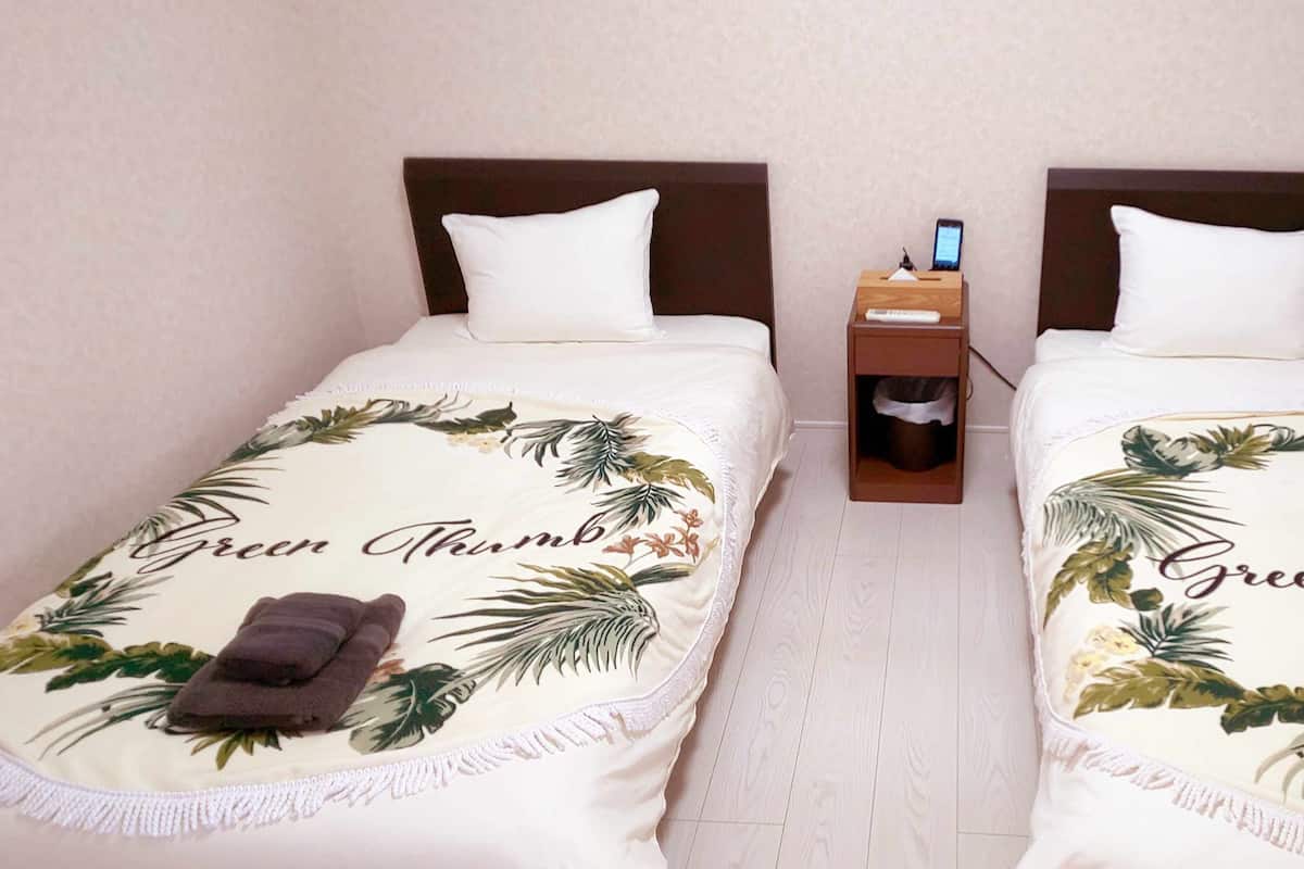 Twee eenpersoonsbedden met passend bloemenbeddengoed en handdoeken, een nachtkastje met telefoon en afstandsbediening, en een witte kast in een hotelkamer.
