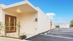 Ein Gebäude mit Flachdach, Holztür und Parkplatz mit eingezeichneten Stellplätzen.