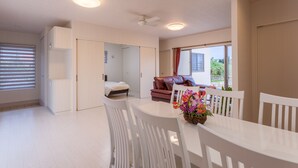 Ein stilvolles, helles Zimmer mit Esstisch, weißen Stühlen, einem braunen Sofa und Deckenventilator.