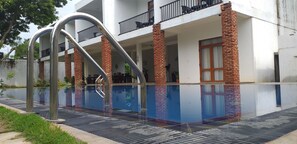 A modern building with a swimming pool, brick pillars, and a balcony with outdoor furniture. - Amelia Resort (Avudangawa)